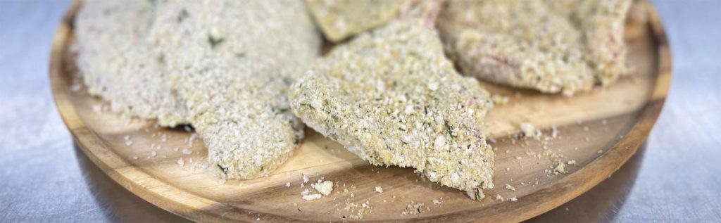 Crunchy breaded chicken schnitzels on a wooden plate, ready for cooking or serving.